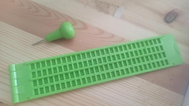 Imagen sobre una madera del kit verde de braille donde está el "punzón" y la plantilla. Ambas de color verde claro posada una al lado de la otra en paralelo