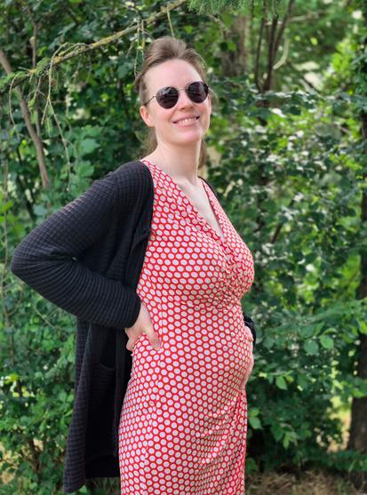It’s a photo of me taken outdoors, wearing a red dress with white polka dots. I’m smiling and proudly showing my baby bump. I’ve just entered my second trimester, so it’s still quite small, but I’m very happy about it.
