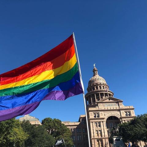 photo of rainbow pride flag flying in front of the Texas State Capitol building in Austin TX