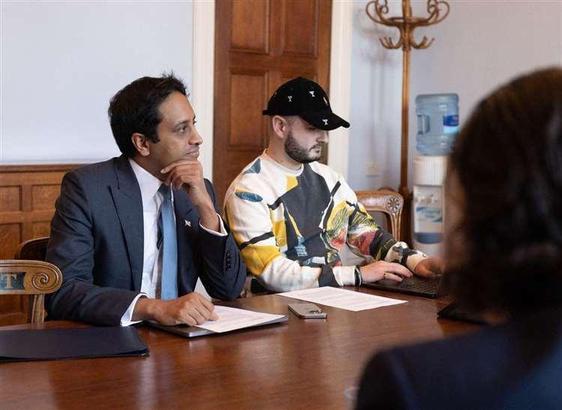 Zia Yousuf looking serious next to Nathaniel Fried who is incongruously wearing bright leather clothing and a peaked baseball cap