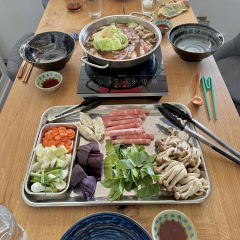 A view of the laid table with the hot pot soup on a cooker and a tray with ingredients.