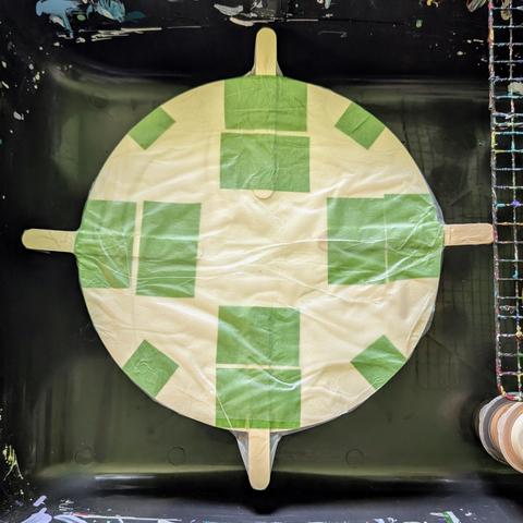 A top view of my paint spinner: there is a circular wooden board with four popsicle sticks taped to it, and the entire thing is covered in GLAD Press'NSeal.