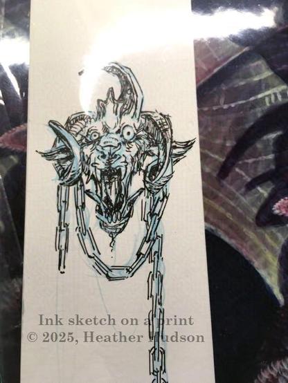Photo of a demon head, with chains, drawn in black ink in the margin of a print by artist Heather Hudson.  Text on photo reads "Ink Sketch on a Print/ ©2025, Heather Hudson."