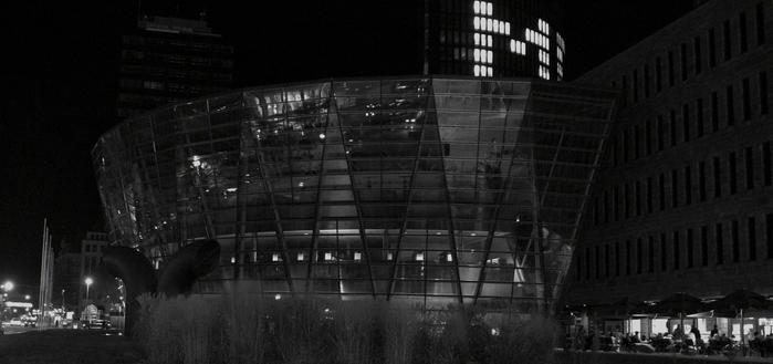 A modern glass building with curved architecture shines in the city at night, while people sit outside a nearby restaurant, surrounded by the urban darkness.

Ein modernes Glasgebaeude mit geschwungener Architektur erstrahlt nachts in der Stadt, waehrend die Menschen vor einem nahe gelegenen Restaurant sitzen, umgeben von der staedtischen Dunkelheit.