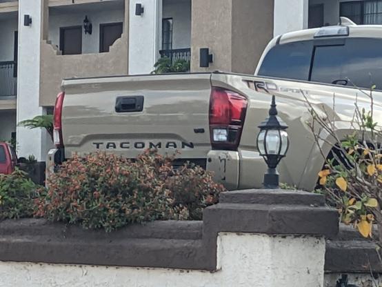 The back of a pickup truck parked in front of a motel. The owner (presumably) has added an N to the Tacoma logo, making it read TACOMAN.