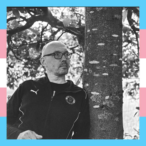 Selbstporträt Toby an einen Baumstamm geleht, St Pauli Jacke, Glatze, entspannter Block nach rechts, Rahmen in Trans Farben