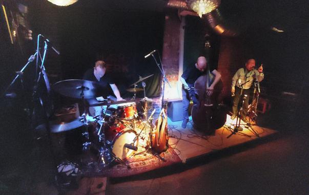 Arashi: 
from left to right: Paal Nilssen-Love playing drums, Johan Berthling playing double bass, Akira Sakata talking, pointing his finger in the air