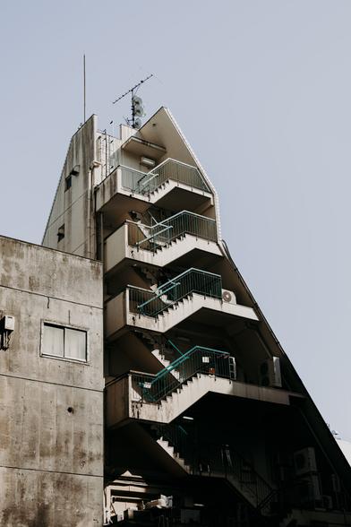 photo of a building with a steep angled side, showing small balconies on the side facing the user. the sun is casting interesting shadows.