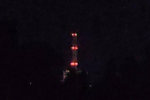 Nachtaufnahme eines Schornsteins des Kohlekraftwerks in Karlsruhe. Es ist alles tiefschwarz, der Schornstein selbst ist gerade so erkennbar. Deutlich zu sehen ist nur die rote Hindernisbefeuerung auf drei Ebenen.