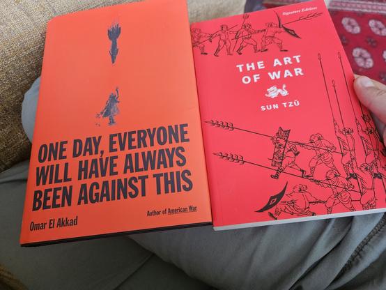 a picture of two books: on the left, One Day, Everyone Will Have Always Been Against This by Omar El Akkad; on the right, The Art of War by Sun Tzu. Both book covers are crimson red.