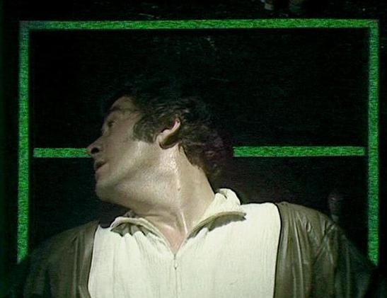 Claude Sonnet 4.0 describes the image as: "I can see this appears to be from a science fiction television production, showing a person in what looks like a white or light-colored shirt or jacket against a dark background with green geometric framing elements. The lighting and visual style is characteristic of 1970s or early 1980s British television production. The setting appears to be some kind of interior space, possibly a spacecraft or futuristic facility, with the distinctive green-tinted geometric design elements that were common in sci-fi productions of that era. The image quality and cinematographic style is typical of the period's television production values."

Blakes7Bot, version 3.9.30.