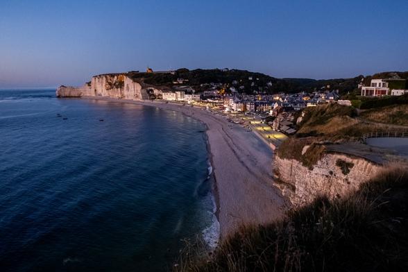 A coastal view at twilight, featuring a beach lined with buildings and cliffs.
