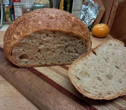a round, light brown loaf sliced open on a cutting board to reveal the sumptuous crumb with bubbles of varied size