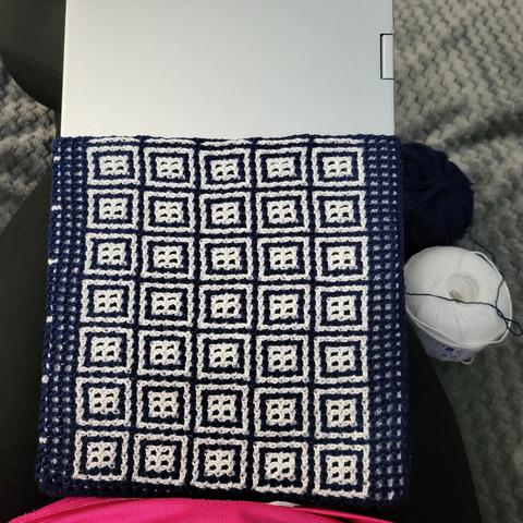 Photo de mon ouvrage en crochet : une housse pour laptop en crochet entrelacé. Le laptop depasse encore car l'ouvrage n'est pas terminé. 
La housse est bleue foncée avec des motifs carrés blancs