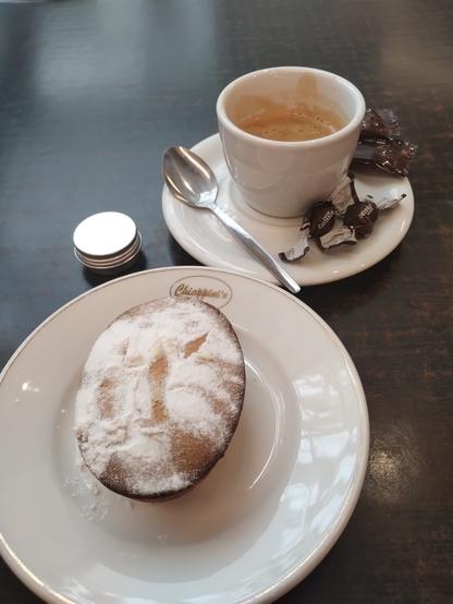 A fresh baked pasticciotto pastry with a double espresso. All in and on plain white crockery. A small silvery tin of mystery contents to the left