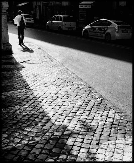 Black and white photo with a man on the top left, at the start of a big opening of light that spans diagonally across the photo. The rest of the photo is dark, elevating the light