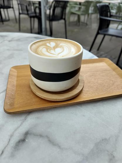 Ein Cappuccino in einer weißschwarzen Tasse auf einem Tisch