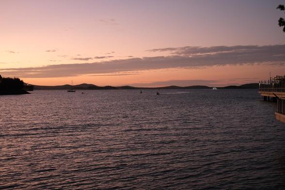Photo of water at dusk the sky has a pink tinge there is a boat motoring in the distance.