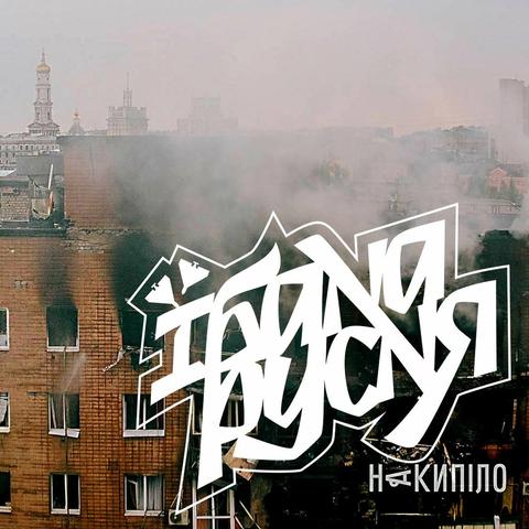 A graffiti-style text overlay in white, Cyrillic script (їбана русня, ie “fucking russians”), is centered over a photograph of a multi-story brick apartment building in Kharkiv, Ukraine, on June 7, 2025, after a Russian bombardment. Black smoke billows from several windows of the burning building. The top of the building is obscured by smoke and the white text. In the background, partially visible above the smoke, are more distant city buildings, including some with prominent domes or spires, characteristic of Kharkiv's architecture. The overall impression is one of urban destruction and artistic commentary in the aftermath of an attack.