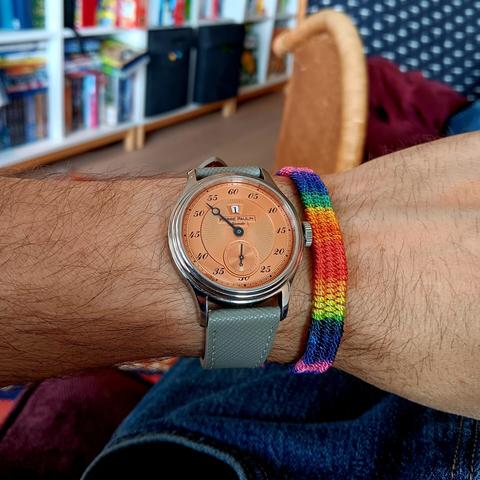 Pinkish (salmon) watch with a gray strap, with a rainbow band on right.