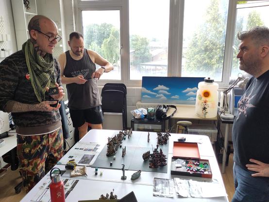 Three people discuss wargaming setup, while shuffling cards.