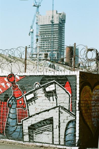 Mural of a menacing robot on a wall, with a skyscraper being built in the background