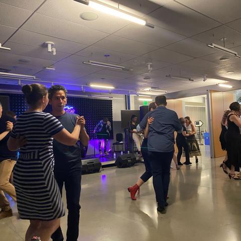 Several dancing couples. In the background, there’s DJ is visible while the cellist checks his equipment.