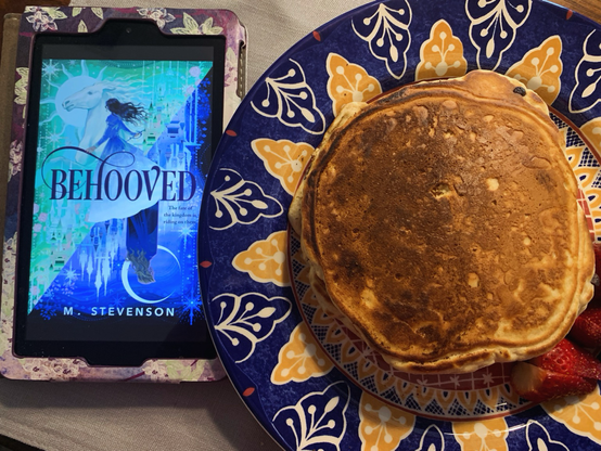 A kindle showing the cover of behooved next to a plate of pancakes