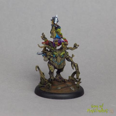 The goblin herself is a dazzling centerpiece: her luminous green skin contrasts brilliantly against her richly colored garments—deep purple trousers, a vivid red sash, a blue scarf fluttering behind her, and a bright turquoise shirt sleeve. Each color pops without clashing, revealing an artist with a fearless sense of palette. Her posture, one arm raised high holding a crude, menacing club adorned with metal shards, evokes power and feral delight. Her face, now visible in fuller detail, is expressive—mouth agape in a shout or cackle, with eyes keen and wild. Beneath her, the wooden steed appears even more animated from this angle. Its face is carved with a mischievous and determined expression—its glowing cyan eyes and jagged wooden brow suggesting a spirit more cunning than brutish. The texture of its bark is lovingly rendered in earthy hues, enriched with mossy green hints and streaks of unnatural blue glowing from crevices—adding a magical undertone. The tendrils, roots, and twisted limbs all feel alive and reactive, as if this creature is both wild beast and ancient guardian.