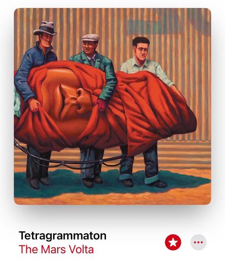 A screenshot of The Mars Volta “Amputechture” album art. A group of three men carrying a large red head, wrapped in a red cloth, stands against a backdrop of vertical stripes.