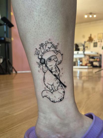 A photo of a tattoo I did on a clients leg of a little witchy lizard wizard holding a staff and wearing a very big hat covered in mushrooms and plants.