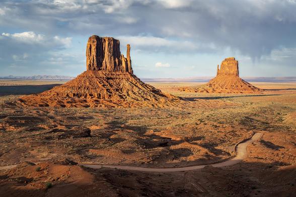 The classic view of the West (left ) and East (right) Mittens rock formations in Monument Valley, Arizona. The road through the tribal park is seen in the foreground.