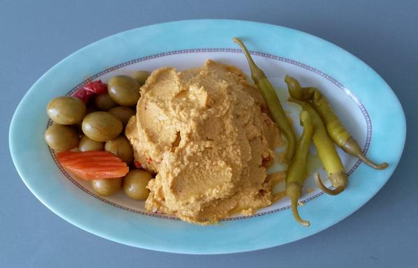 En un plato ovalado pequeño unas aceitunas, un montoncito de hummus y unas piparras.