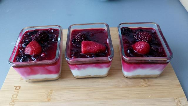 Tres cuencos de cristal rectangulares pequeños. En cada uno de ellos hay un postre con frutos rojos por encima.