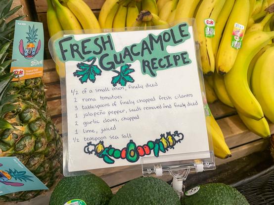 Laminated recipe near bananas, pineapple, and avocados that calls for onion, tomatoes, cilantro, jalapeño, garlic, lime juice, and sea salt.