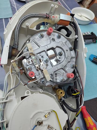 Eine geöffnete Bügelstation, man sieht den Druckkessel, eine Pumpe und ein Magnetventile, die mit Schläuchen und Kabeln verbunden sind