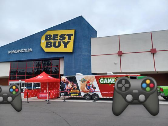 Nintendo Switch 2 demo event in front of Best Buy in Torrance, California on June 7, 2025. There is a red Nintendo Switch 2 tent, and a long trailer thing with Donkey Kong and Mario Kart and the company organizing it (Game Truck?) emblazoned on the visible side.

People have been covered with controller emojis, at the trailer's door and leaving the store.