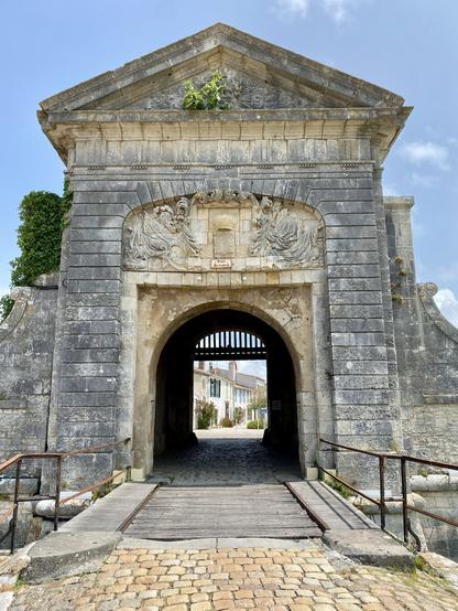 A stone portal from the 1700 century leads in to the city of Saint Martin de Rè. Buildings in the city can be seen through the portal.