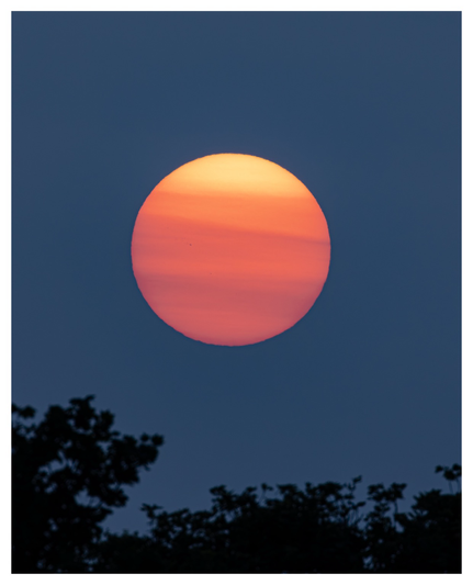 A banded orange orb of the setting sun sitting low in a grey-blue sky. Smoke from wildfires in Canada has crossed the Atlantic, resulting in an otherworldly sunset.