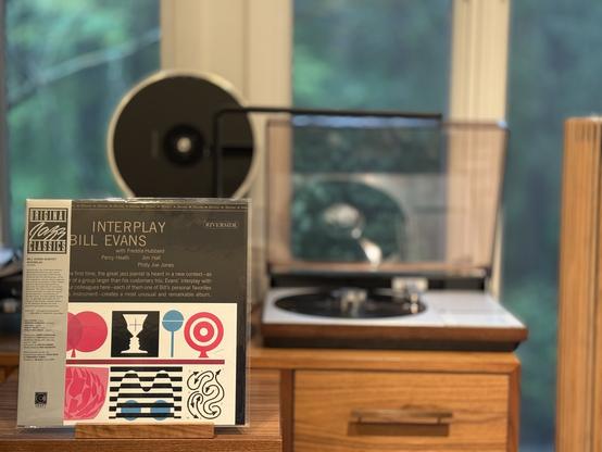 Bill Evans - Interplay LP cover.

Top half with title and artists grey-on-black, below varies shapes and the like on a white background.

The black LP plays on a vintage, restored Bang & Olufsen Beogram 4000 linear-tracking turntable to the right.