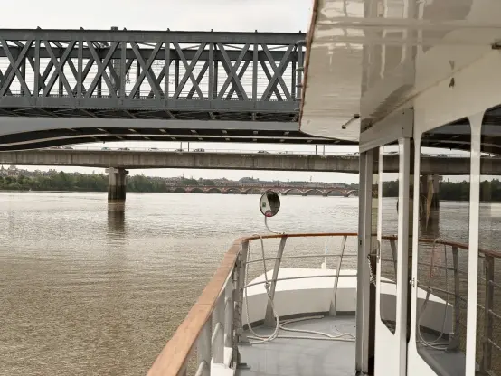 La passerelle férroviaire et les ponts Saint-Jean et de pierre vus depuis un bateau, qui occupe la moitié du premier plan.