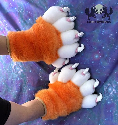 Orange, white, and black fursuit hands with big padded fingers and large white claws with pink cuticles. The pawpads are tan in color and stuffed so they stick out, and the palms are black. The hands are displayed in front of a blue-violet space themed backdrop.