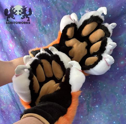 Orange, white, and black fursuit hands with big padded fingers and large white claws with pink cuticles. The pawpads are tan in color and stuffed so they stick out, and the palms are black. The hands are displayed in front of a blue-violet space themed backdrop.