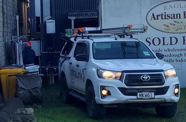 Corner of yard with a container and a ute closing off a small space. In this space a person is working on a switchboard. The ute is running with the exhaust pointed at the worker.
