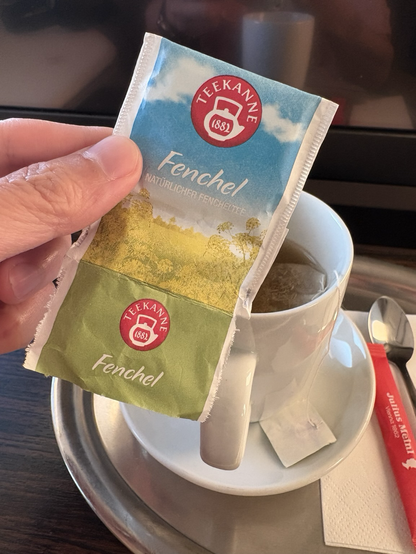 A fennel tea bag wrapper (in German) in front of a cup of fennel tea