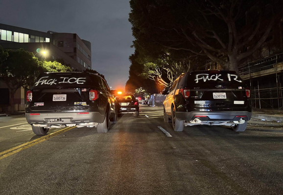 Two police cars, with graffiti on them reading "Fuck ICE" and "Fuck 12."