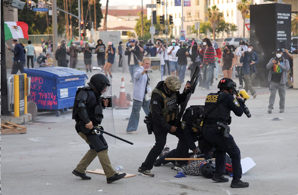 Riot Police brutalize a protester in L.A. after he had been trying to escort a woman out of harm's way using a shield defensively and never touching any police. The protester is already down on the ground after being knocked down from behind by a riot cop.