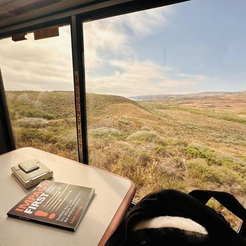 A photo of Matt LeMay’s Impact-First Product Teams book on the observation car table, with a view of outside