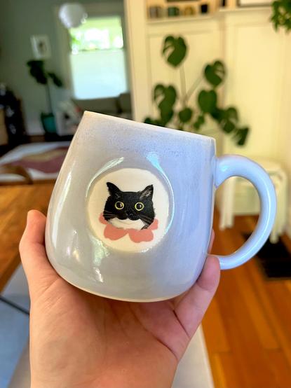 A handmade blue ceramic mug with a cute cat face painted onto it