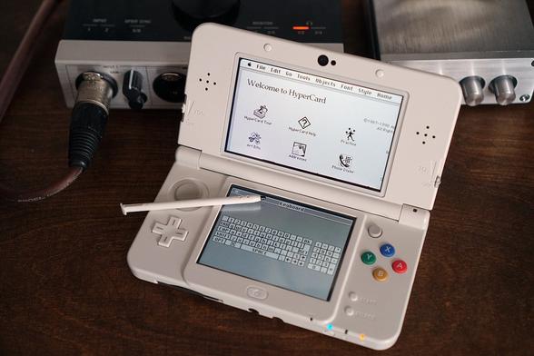 A white Nintendo 3DS sits open in front of some kind of unrelated audio equipment. On its bottom screen is the onscreen Keyboard app for use with the stylus. On the top screen, HyperCard displays the home stack.

It's classy every day in @nomand 's land